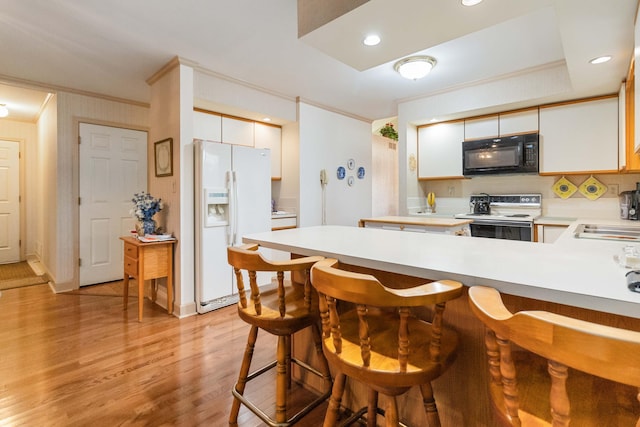 kitchen featuring a kitchen breakfast bar, white appliances, crown molding, white cabinetry, and kitchen peninsula