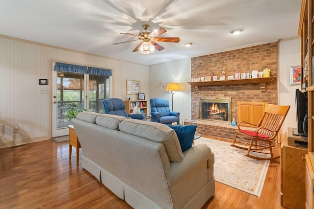 living room with hardwood / wood-style flooring, ceiling fan, crown molding, and a brick fireplace