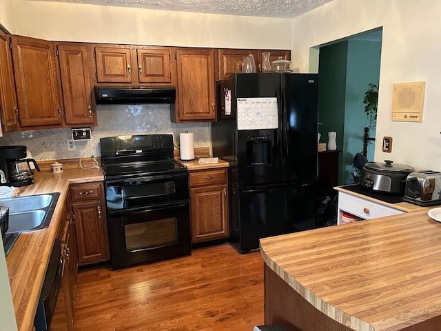 kitchen featuring wood finished floors, under cabinet range hood, a textured ceiling, black appliances, and a sink