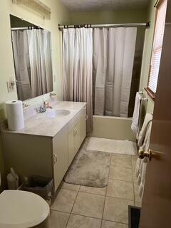 bathroom featuring a textured ceiling, tile patterned flooring, toilet, vanity, and shower / tub combo with curtain