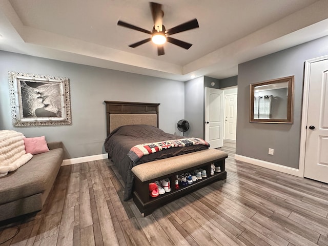 bedroom with a tray ceiling, hardwood / wood-style flooring, a ceiling fan, and baseboards