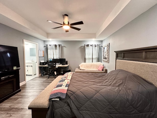 bedroom featuring ceiling fan, a tray ceiling, baseboards, and wood finished floors