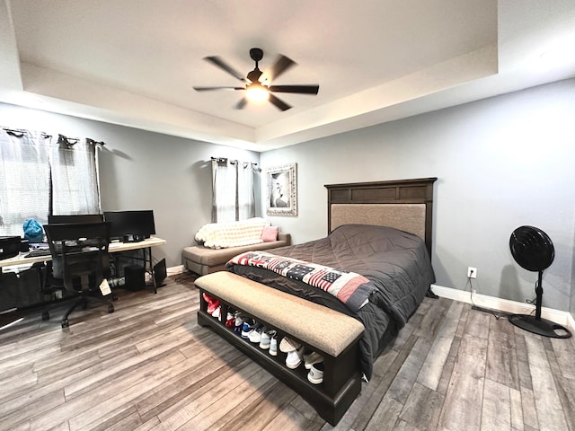 bedroom featuring a raised ceiling, baseboards, and wood finished floors