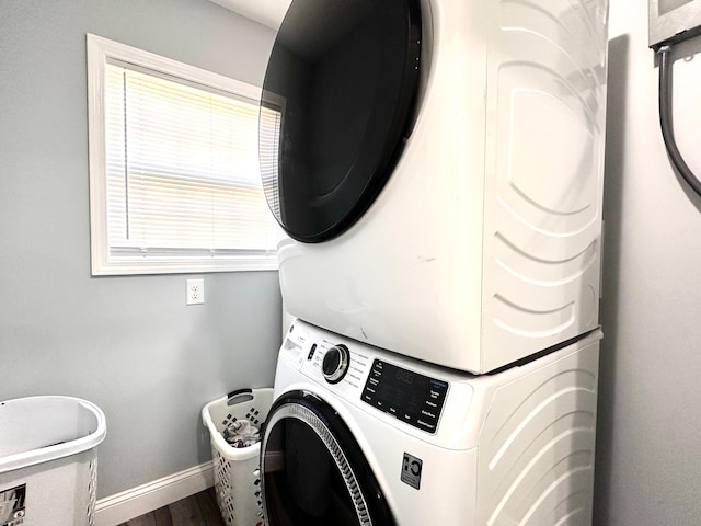 washroom featuring dark wood finished floors, laundry area, baseboards, and stacked washing maching and dryer