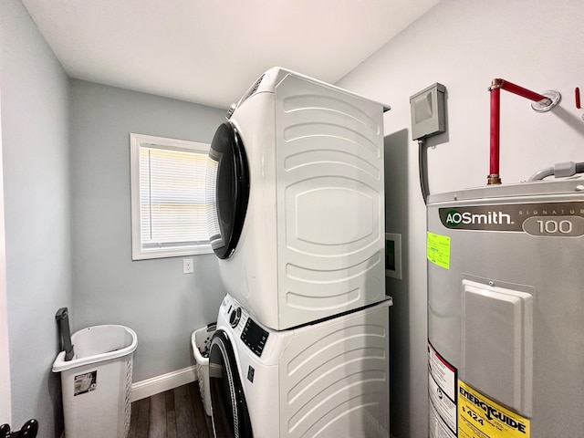 washroom featuring baseboards, water heater, laundry area, stacked washer and clothes dryer, and wood finished floors