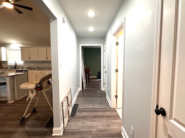 hall with visible vents, baseboards, and dark wood-style flooring