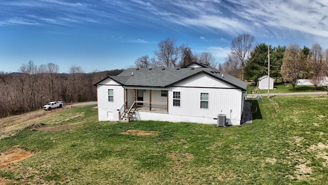 back of property featuring a lawn, a view of trees, and central AC