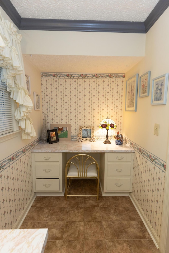 unfurnished office with crown molding, built in desk, dark tile patterned floors, and a textured ceiling