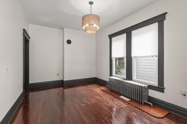 empty room featuring radiator heating unit, dark hardwood / wood-style floors, and a chandelier