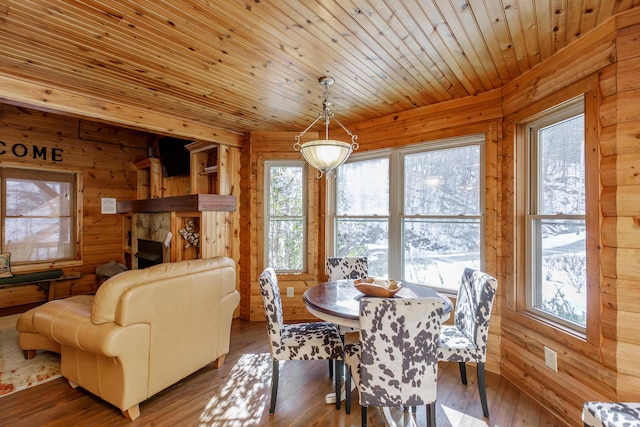 dining area featuring wood ceiling, wood-type flooring, wooden walls, and a stone fireplace