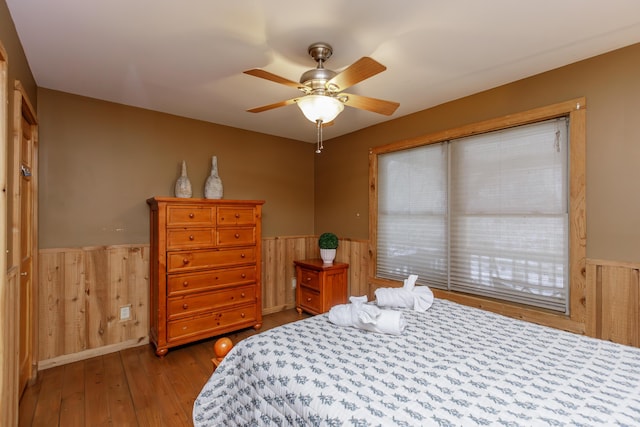 bedroom featuring hardwood / wood-style floors, wooden walls, and ceiling fan