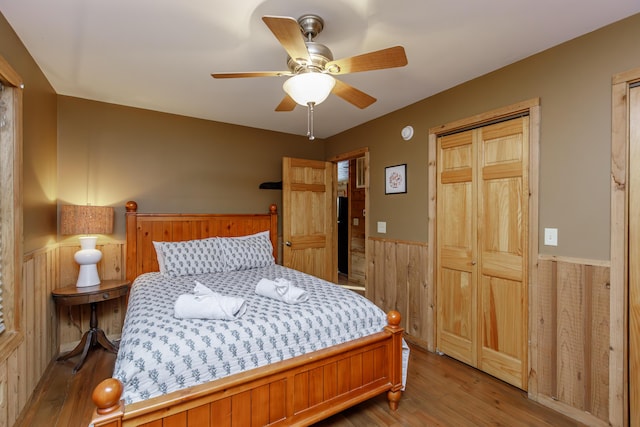 bedroom with wood-type flooring, wood walls, ceiling fan, and a closet