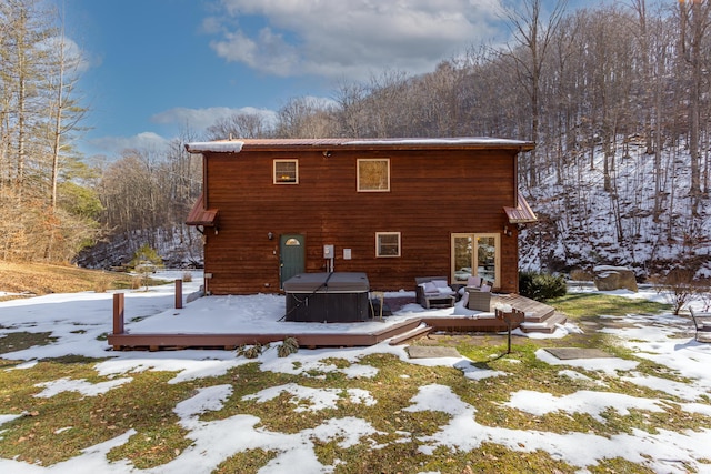 snow covered back of property featuring a wooden deck and a hot tub