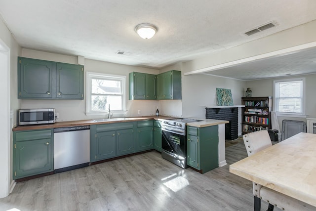 kitchen with sink, green cabinetry, appliances with stainless steel finishes, kitchen peninsula, and light hardwood / wood-style floors