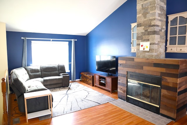 living room featuring lofted ceiling, a large fireplace, and wood finished floors