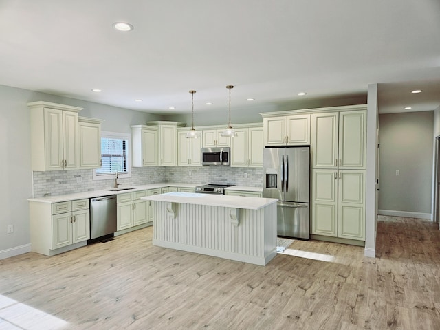 kitchen featuring stainless steel appliances, a sink, hanging light fixtures, light countertops, and a center island