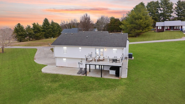 back house at dusk with a patio, a lawn, and a wooden deck