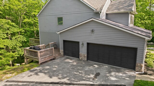 view of side of home with a shingled roof, an attached garage, stone siding, and driveway