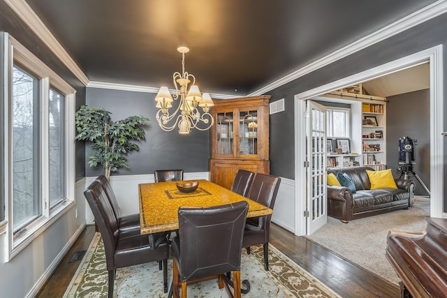 dining space with dark wood-style flooring, a chandelier, ornamental molding, and wainscoting