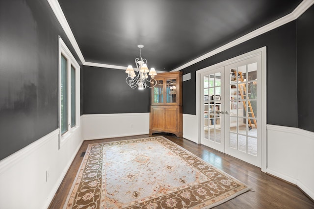 unfurnished dining area featuring french doors, ornamental molding, wood finished floors, wainscoting, and a chandelier