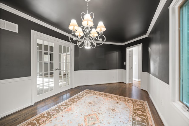 unfurnished dining area with a chandelier, wood finished floors, a wainscoted wall, ornamental molding, and french doors