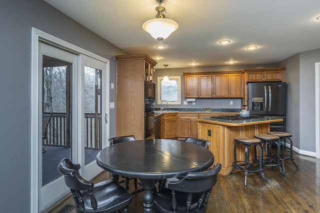 kitchen with refrigerator with ice dispenser, black microwave, baseboards, brown cabinets, and a sink