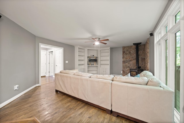 living area with a wood stove, ceiling fan, wood finished floors, and baseboards