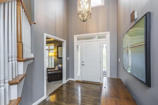 entryway with a towering ceiling, healthy amount of natural light, stairway, a chandelier, and wood finished floors