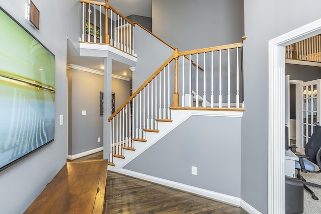 staircase featuring a towering ceiling, ornamental molding, wood finished floors, and baseboards