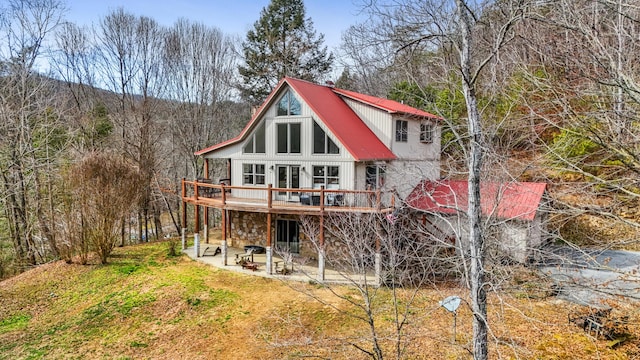 back of house featuring metal roof, stone siding, a patio area, and a wooden deck