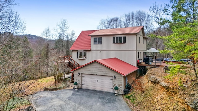 view of front of house with a garage, metal roof, a deck, and a view of trees