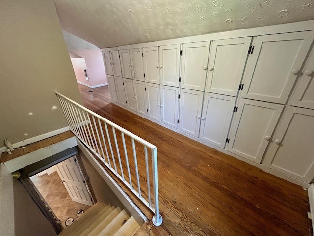 staircase with hardwood / wood-style flooring, vaulted ceiling, and a textured ceiling