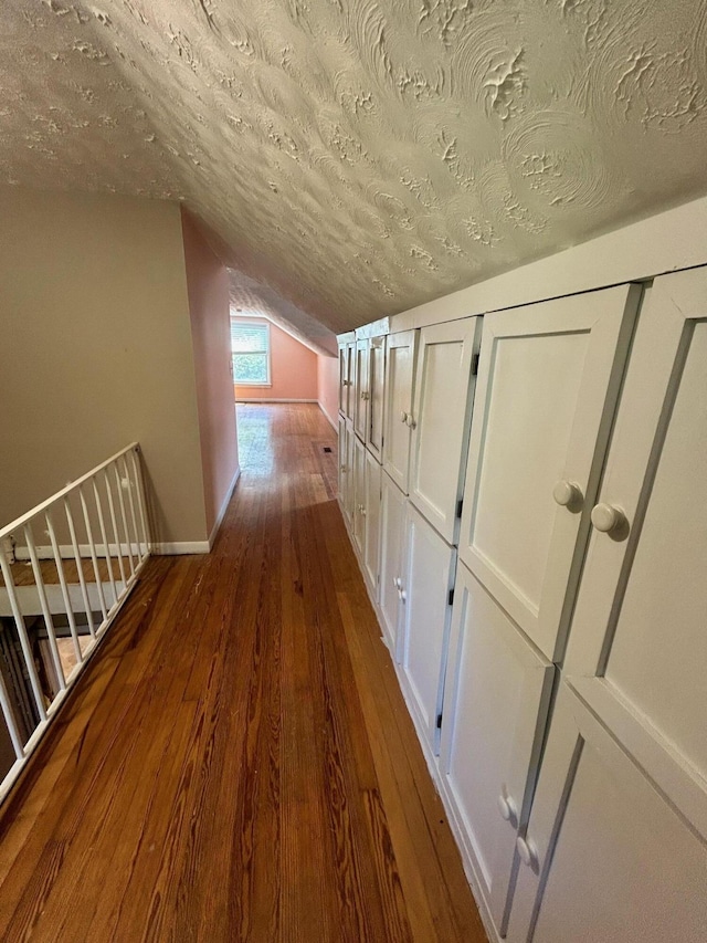 hallway featuring lofted ceiling, dark hardwood / wood-style flooring, and a textured ceiling