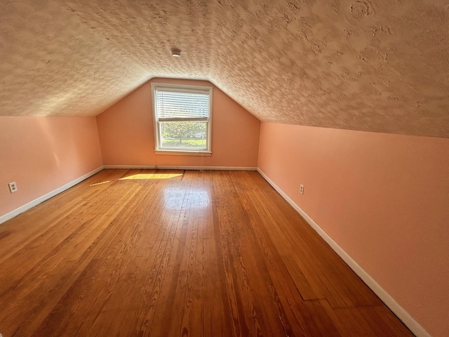 additional living space featuring lofted ceiling, hardwood / wood-style flooring, and a textured ceiling