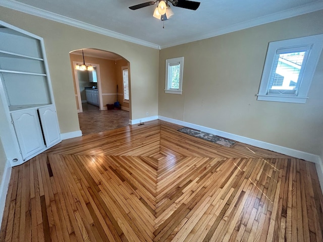 empty room with crown molding, a wealth of natural light, and ceiling fan with notable chandelier