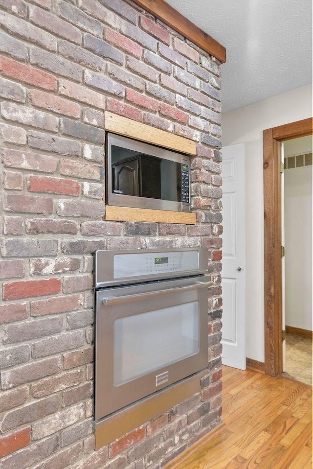 room details with light wood-type flooring, appliances with stainless steel finishes, and a textured ceiling