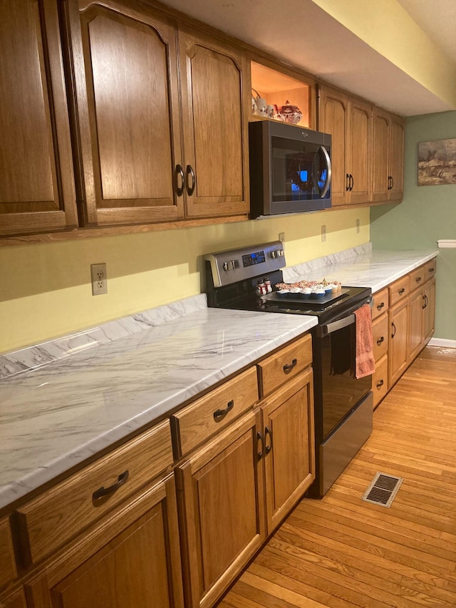 kitchen featuring visible vents, light wood-type flooring, stainless steel microwave, brown cabinetry, and black range with electric stovetop