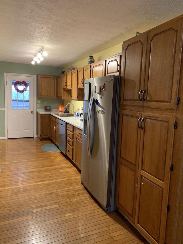 kitchen featuring light wood-style flooring, a textured ceiling, light countertops, stainless steel appliances, and a sink