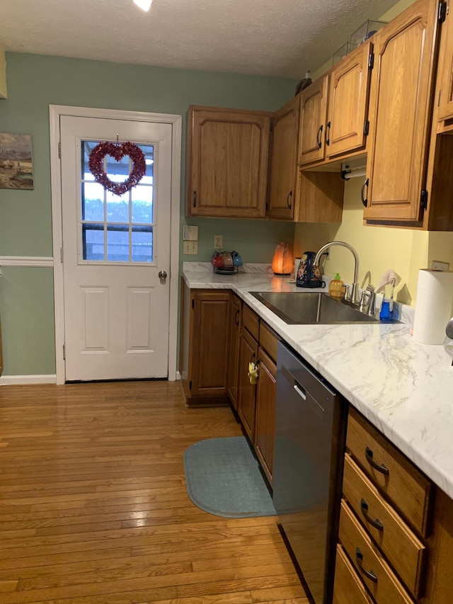 kitchen with dishwasher, light countertops, a sink, light wood finished floors, and baseboards