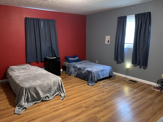 bedroom featuring baseboards, wood finished floors, and a textured ceiling