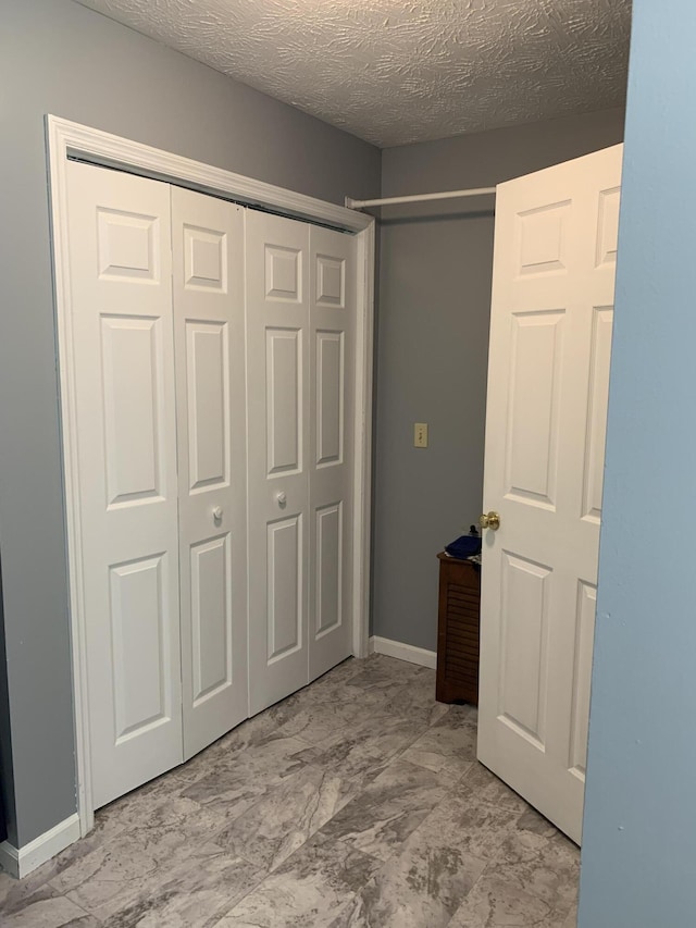unfurnished bedroom with a textured ceiling, a closet, marble finish floor, and baseboards