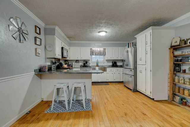 kitchen featuring white cabinetry, ornamental molding, kitchen peninsula, and stainless steel refrigerator