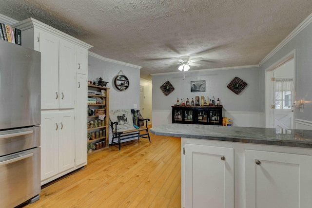 kitchen with white cabinetry, ornamental molding, stainless steel fridge, and light wood-type flooring