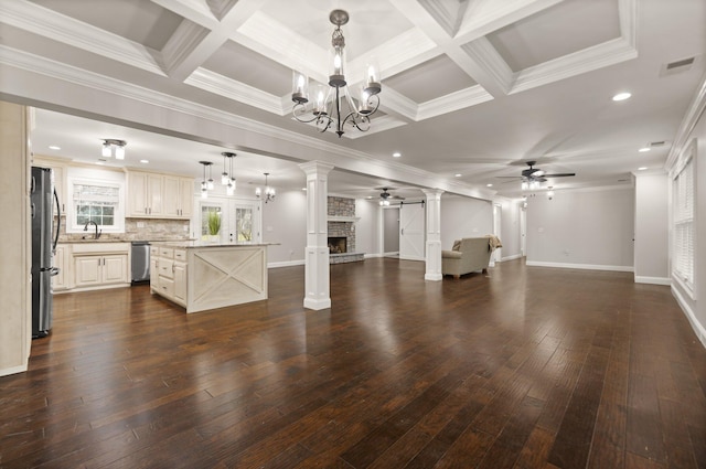 unfurnished living room with ornate columns, dark hardwood / wood-style floors, ceiling fan with notable chandelier, a fireplace, and sink