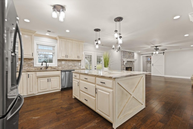 kitchen featuring appliances with stainless steel finishes, light stone counters, cream cabinets, a kitchen island, and decorative light fixtures