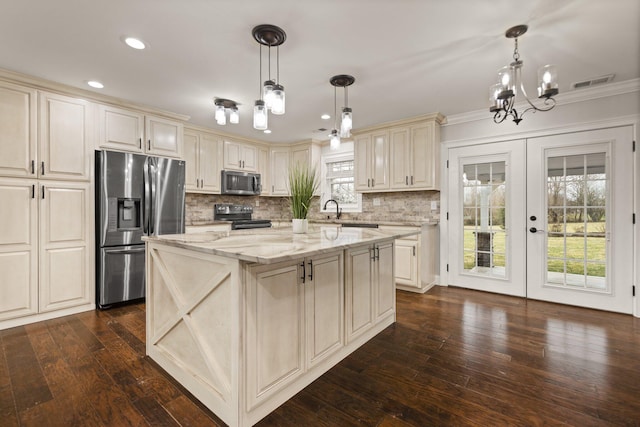 kitchen featuring a kitchen island, hanging light fixtures, light stone counters, stainless steel appliances, and cream cabinets