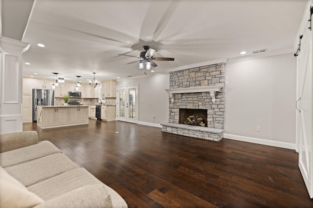 living room with ceiling fan with notable chandelier, a fireplace, ornamental molding, and dark hardwood / wood-style floors