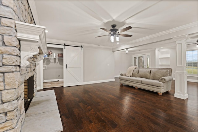 living room featuring ceiling fan, ornamental molding, a barn door, and decorative columns