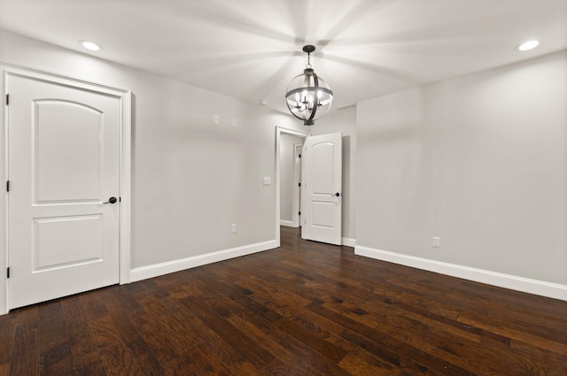 spare room featuring dark wood-type flooring and a chandelier