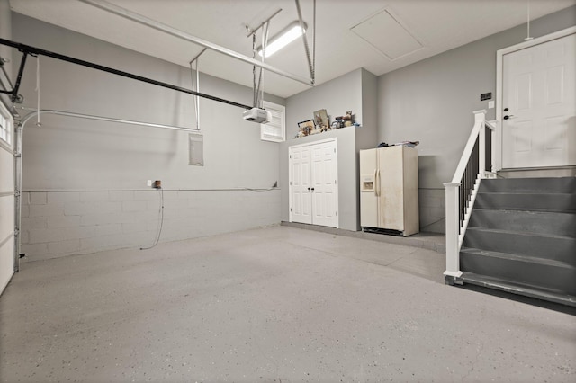 garage with a garage door opener and white refrigerator with ice dispenser